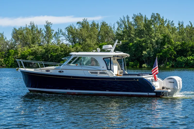 Slide: The Image of 2020 Back Cove 340 boat cruising on a serene lake with lush greenery. - 47