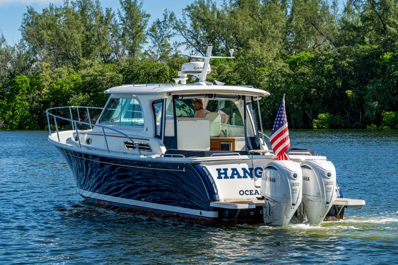 Slide: The Image of 2020 Back Cove 340 boat cruising on a scenic waterway with lush greenery. - 49