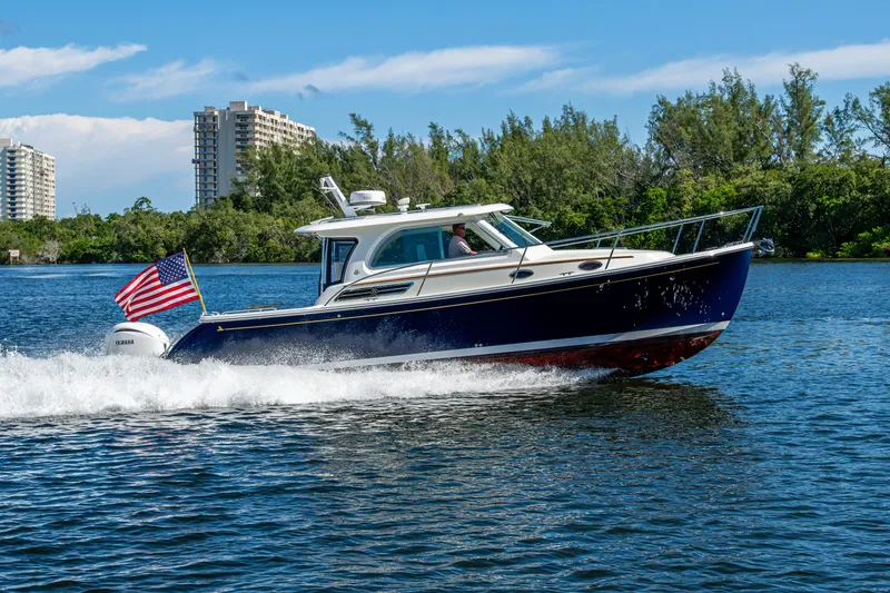 Slide: The Image of 2020 Back Cove 340 boat cruising on water with American flag, cityscape background. - 67