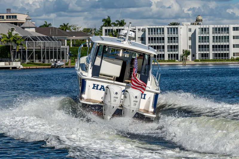 Slide: The Image of 2020 Back Cove 340 boat cruising on water with American flag, modern buildings in background. - 76