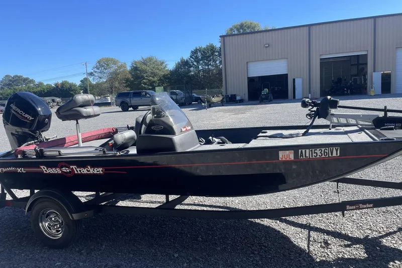 Slide: The Image of 2024 Bass Tracker Classic XL boat with Mercury engine, parked outdoors near a warehouse. - 6