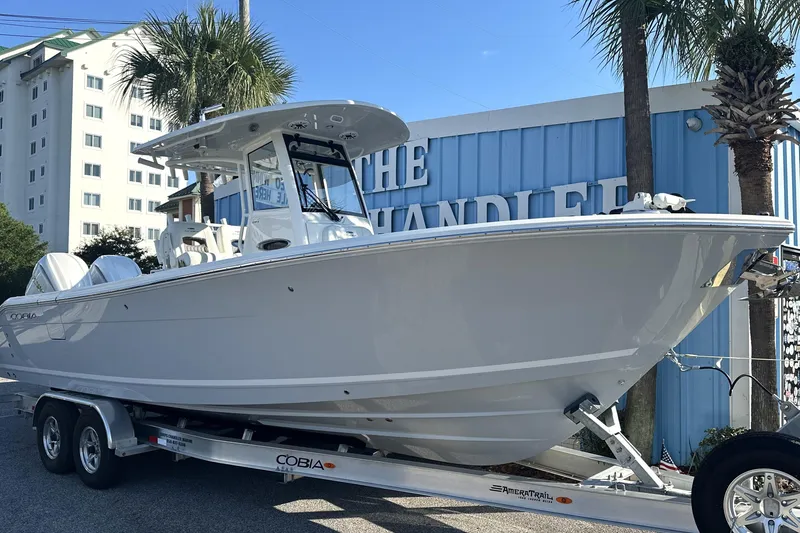 Slide: The Image of 2026 Cobia 285 Open Center Console boat on trailer, parked near a building with palm trees. - 4