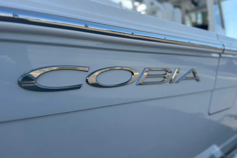 Slide: The Image of 2026 Cobia 285 Open Center Console boat, close-up of logo on sleek white hull. - 6