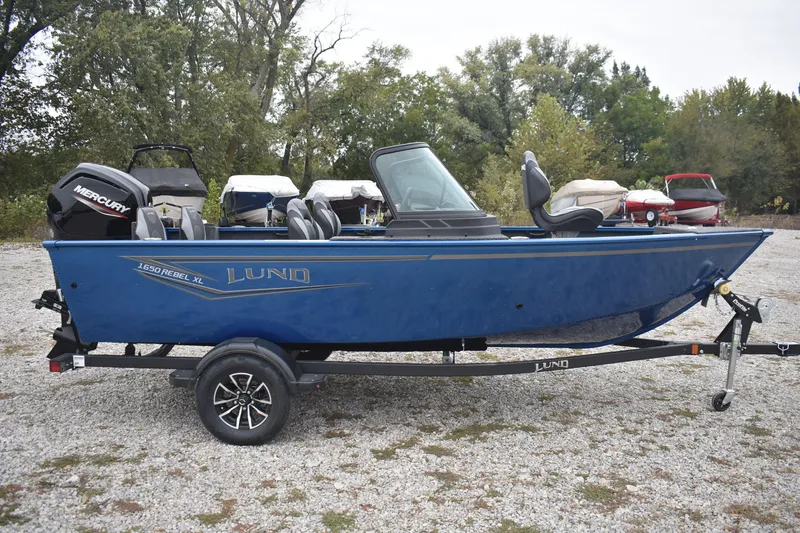 Slide: The Image of 2026 Lund 1650 Rebel XL Sport boat on trailer, blue exterior, parked outdoors. - 1