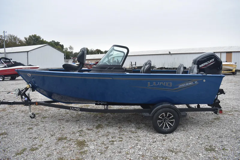 Slide: The Image of 2026 Lund 1650 Rebel XL Sport boat on trailer, blue exterior, parked outdoors. - 5