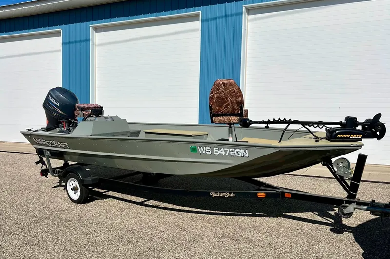 The Image of 2004 MirroCraft 1876 Outfitter boat with Yamaha motor on trailer, parked outside blue building. - 1