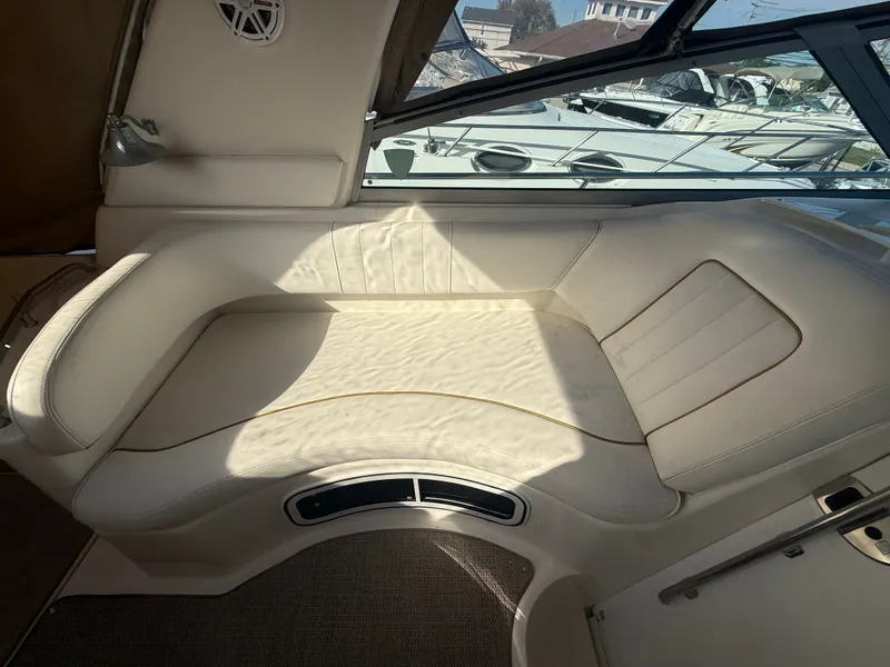 Slide: The Image of Interior seating of 2001 Sea Ray 290 Sundancer boat, featuring cream upholstery and window view. - 10
