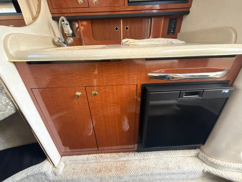 Slide: The Image of 2001 Sea Ray 290 Sundancer interior kitchenette with wood cabinets and compact fridge. - 22