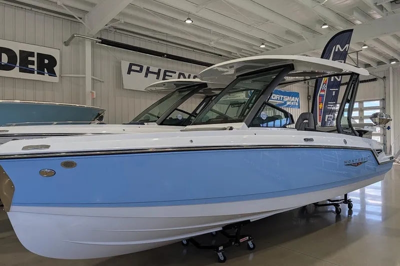The Image of 2026 Monterey Elite 25 OB boat displayed indoors, featuring sleek design and blue accents. - 1