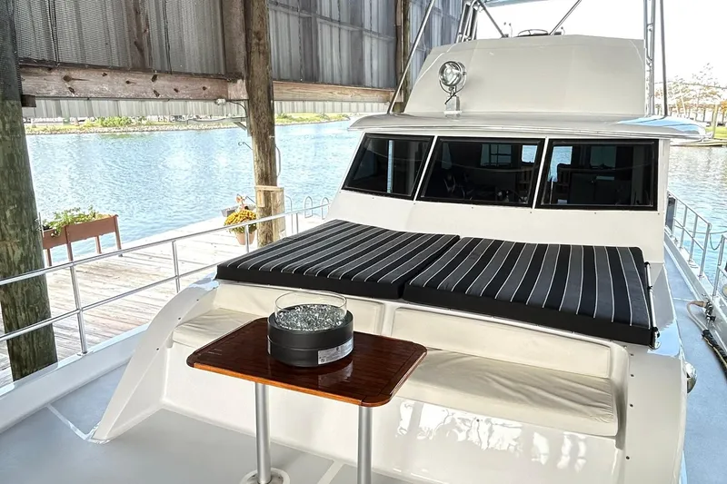 Slide: The Image of 1979 Hatteras 53 Motor Yacht Hard Top with striped cushions and table, docked by the water. - 112