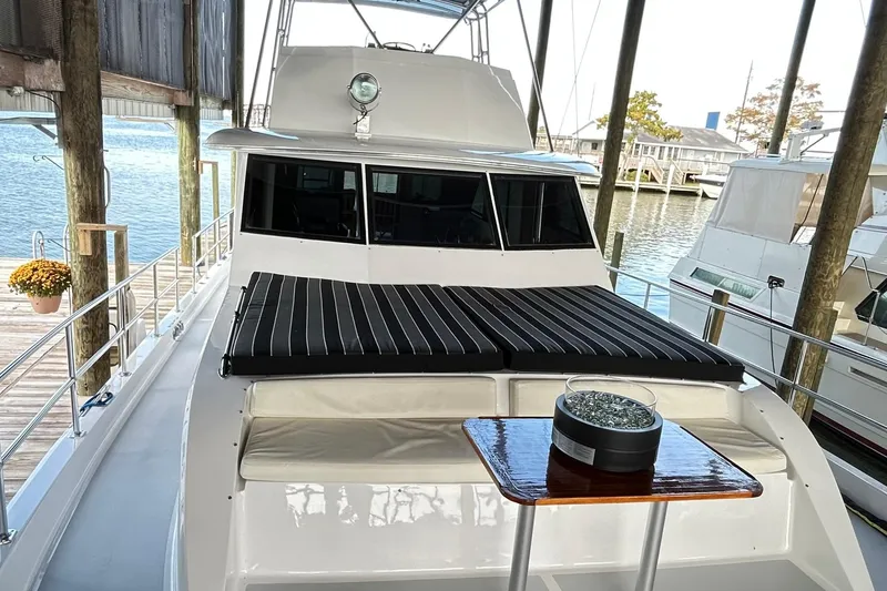Slide: The Image of 1979 Hatteras 53 Motor Yacht Hard Top docked, featuring striped cushions and a small table. - 113