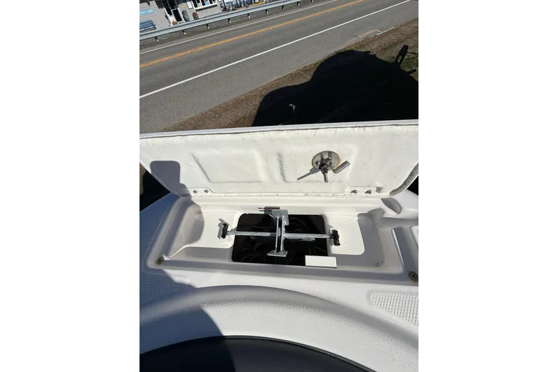 Slide: The Image of 2021 Robalo R222 Explorer anchor storage compartment with open lid, showing anchor and road in background. - 11