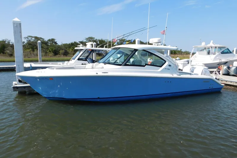 Slide: The Image of 2024 Pursuit DC 326 Dual Console boat docked in a marina, featuring a sleek blue hull. - 101