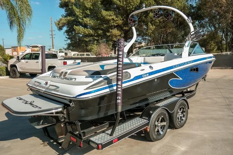Slide: The Image of 2014 Centurion Enzo SV233 boat on trailer, parked outdoors, with wakeboard tower and blue accents. - 5