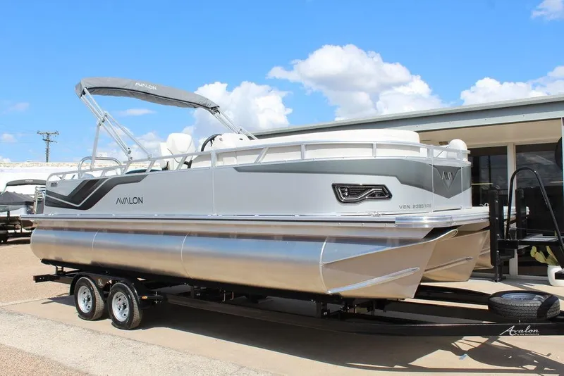 The Image of 2025 Avalon Venture 85 Versatile Rear Bench 23 FT pontoon boat on trailer, under blue sky. - 1