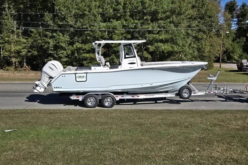 Slide: The Image of 2026 Sea Hunt Ultra 285 SE boat on trailer, parked roadside with trees in background. - 34