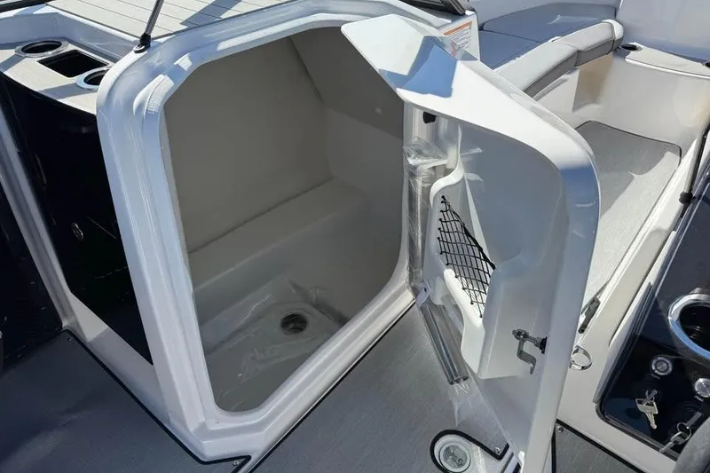 Slide: The Image of 2026 Yamaha Boats AR250 interior storage compartment with open door and cup holders. - 14
