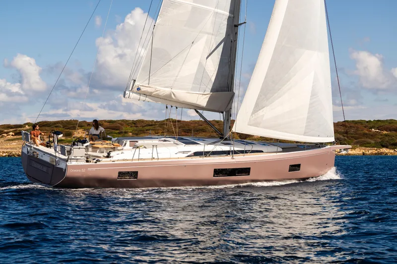 The Image of 2026 Beneteau Oceanis 52 sailing yacht on open water, clear skies, and scenic coastline. - 0
