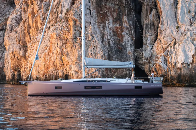 Slide: The Image of 2026 Beneteau Oceanis 52 yacht sailing near rocky cliffs at sunset. - 2