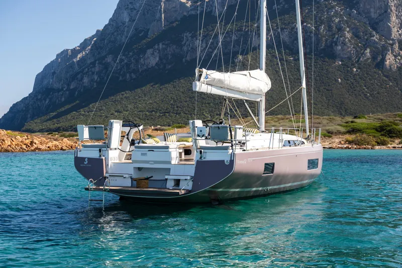 Slide: The Image of 2026 Beneteau Oceanis 52 yacht anchored in clear turquoise waters near rocky coastline. - 4