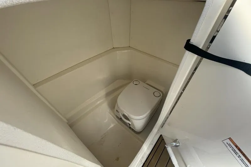 Slide: The Image of 2024 Sea Ray 230 Sportster Bow Rider interior with compact marine toilet. - 8