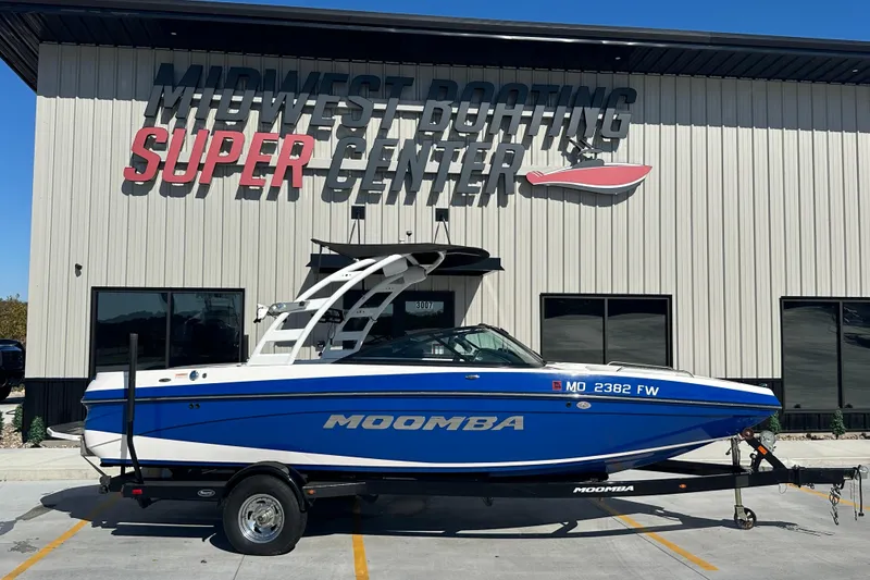 Slide: The Image of 2015 Moomba Mobius LSV boat in blue and white, parked outside a building. - 3