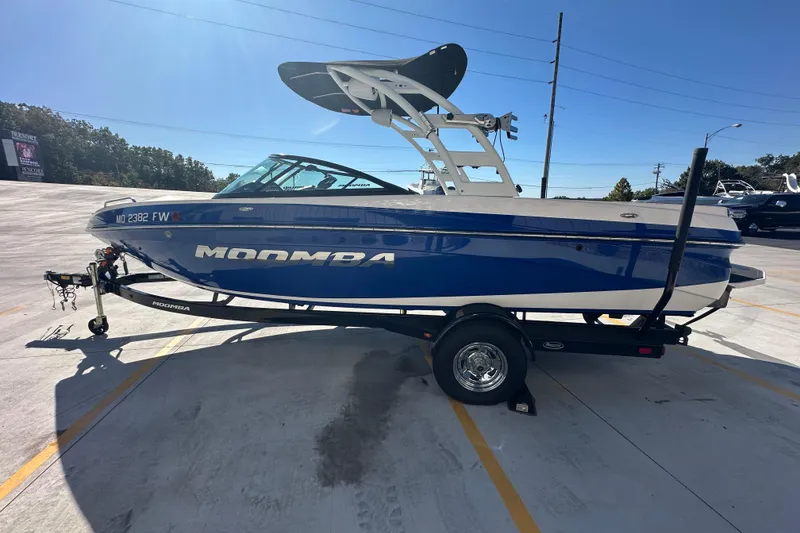 Slide: The Image of 2015 Moomba Mobius LSV boat with blue and white design, parked outdoors. - 8