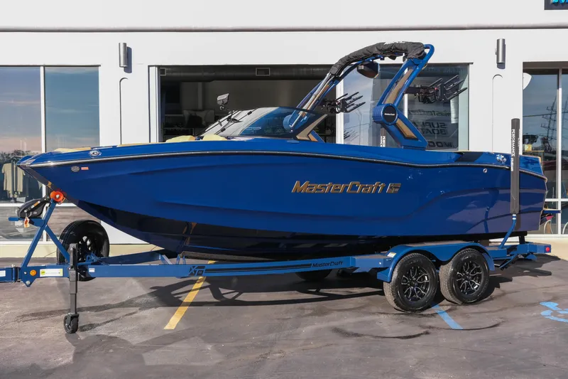 Slide: The Image of 2026 MasterCraft XT22 boat in blue on a trailer, parked outside a building. - 2