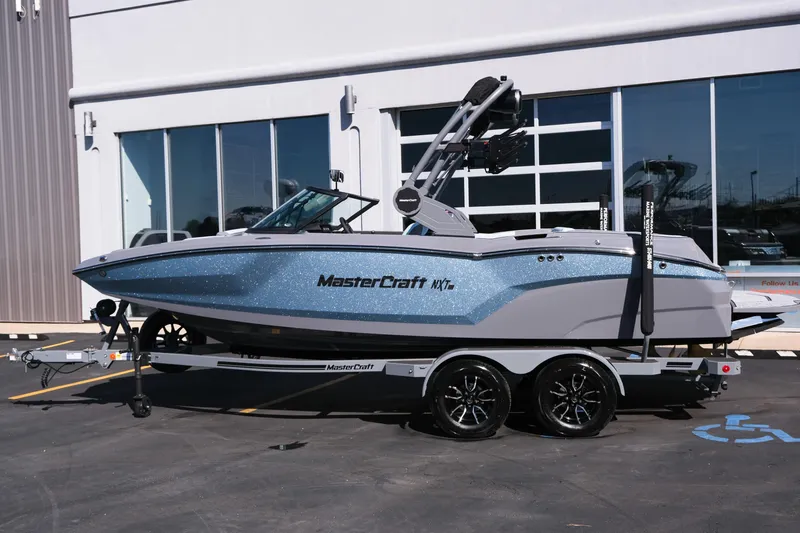 Slide: The Image of 2026 MasterCraft NXT20 boat on trailer, parked outside a modern building. - 18