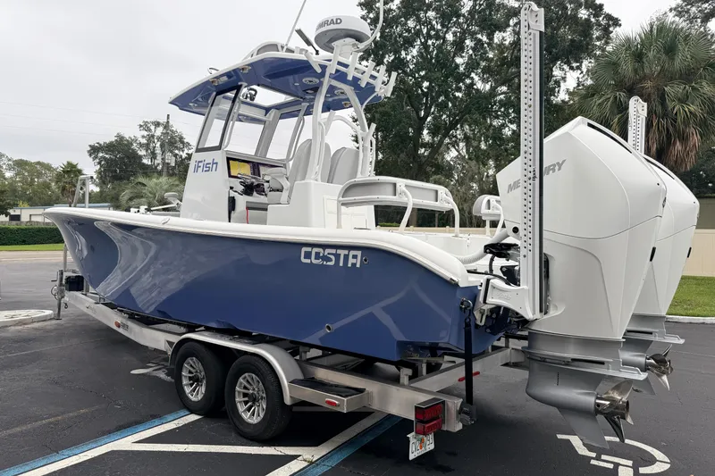 Slide: The Image of 2022 Costa Custom Boats 264 on trailer, blue hull, dual Mercury engines, parked outdoors. - 2