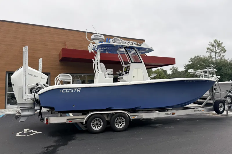 Slide: The Image of 2022 Costa Custom Boats 264 on trailer, blue hull, parked outside a building. - 5