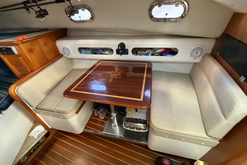 Slide: The Image of 2004 Pursuit 3100 Offshore cabin with wooden table, cushioned seating, and storage compartments. - 19