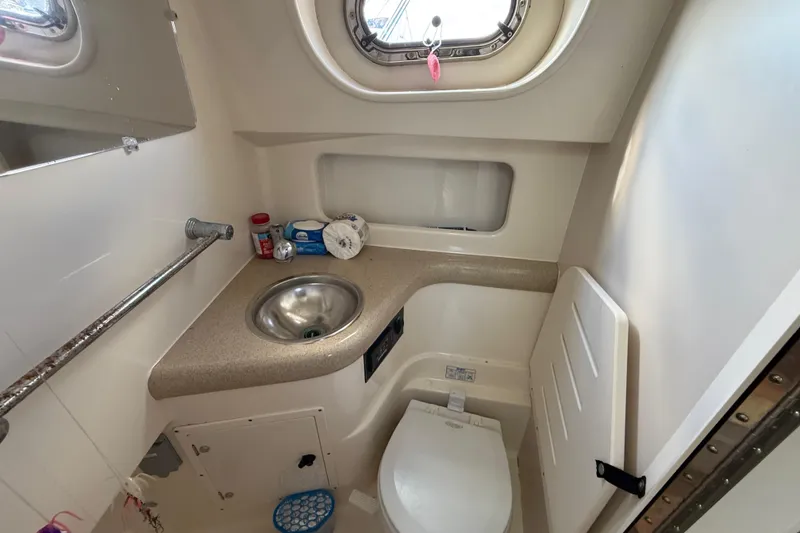 Slide: The Image of 2004 Pursuit 3100 Offshore boat bathroom with sink, toilet, and porthole window. - 26