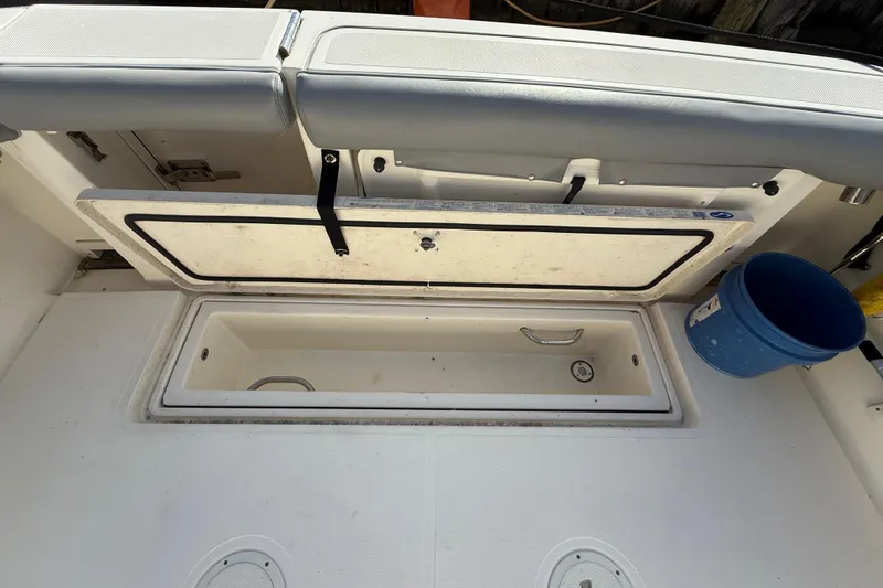 Slide: The Image of 2004 Pursuit 3100 Offshore boat interior with open storage compartment and blue bucket. - 38