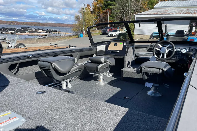 Slide: The Image of 2026 Lund 1875 Crossover XS boat interior with seating and steering wheel, dockside view. - 10