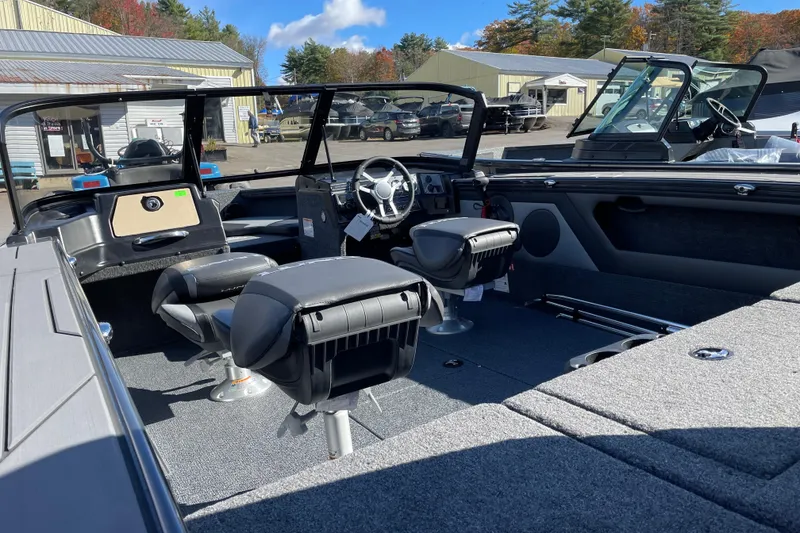 Slide: The Image of 2026 Lund 1875 Crossover XS boat interior with seating and steering wheel, parked outdoors. - 11