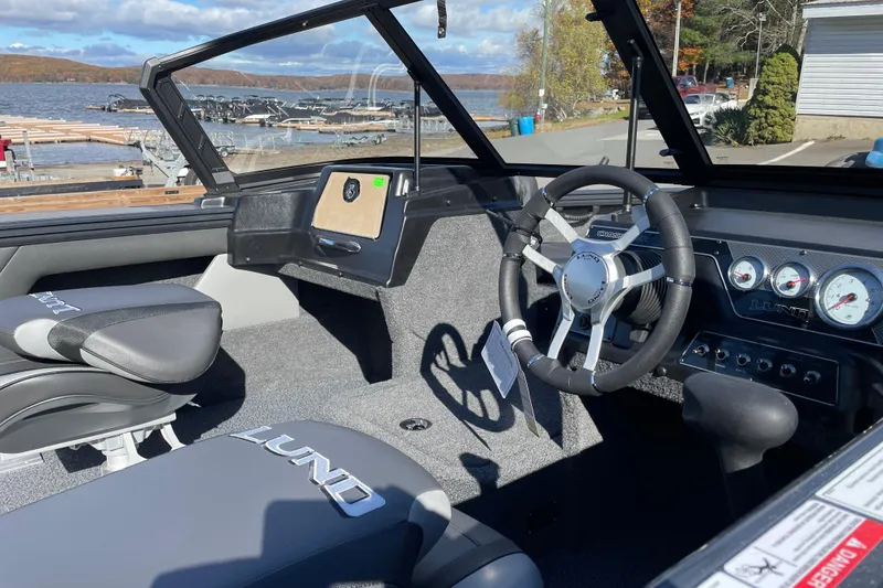 Slide: The Image of 2026 Lund 1875 Crossover XS boat interior with steering wheel and dashboard, dockside view. - 7