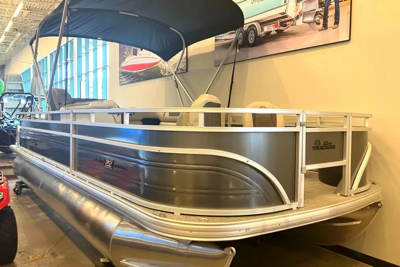 The Image of A 2026 Sun Tracker Fishin' Barge 22 DLX pontoon boat is displayed in a showroom. - 0