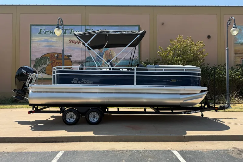 The Image of 2026 Sun Tracker SportFish 22 DLX pontoon boat on trailer, parked outdoors. - 0