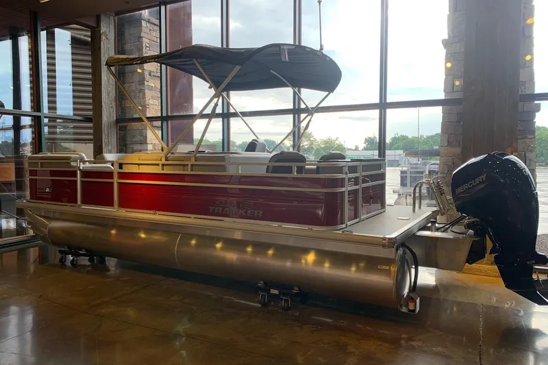 The Image of 2026 Sun Tracker SportFish 22 DLX pontoon boat displayed indoors with Mercury engine. - 0