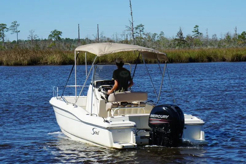 Slide: The Image of 2015 Scout 215 XSF boat cruising on a calm river with a Mercury outboard motor. - 17