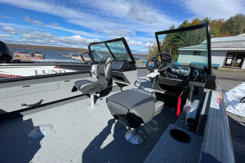 Slide: The Image of 2026 Lund 1775 Adventure Sport boat interior with steering wheel and seats, docked by a scenic lake. - 8
