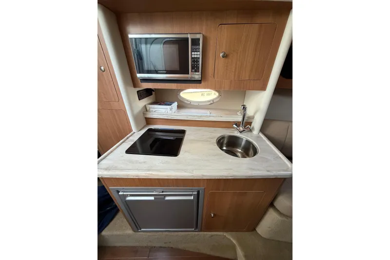 Slide: The Image of 2015 Rinker 290 Express Cruiser kitchenette with microwave, sink, and stovetop. - 8