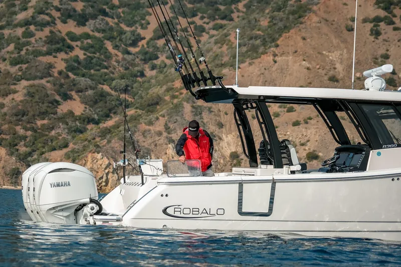 Slide: The Image of 2025 Robalo R360 Center Console boat with Yamaha engines, man fishing near rocky coastline. - 20