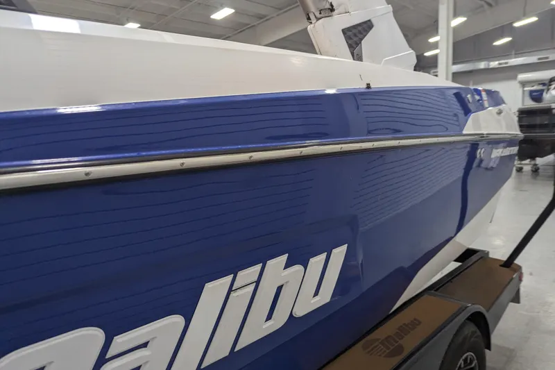 Slide: The Image of 2021 Malibu Wakesetter 22 LSV boat in a showroom, blue and white exterior. - 16