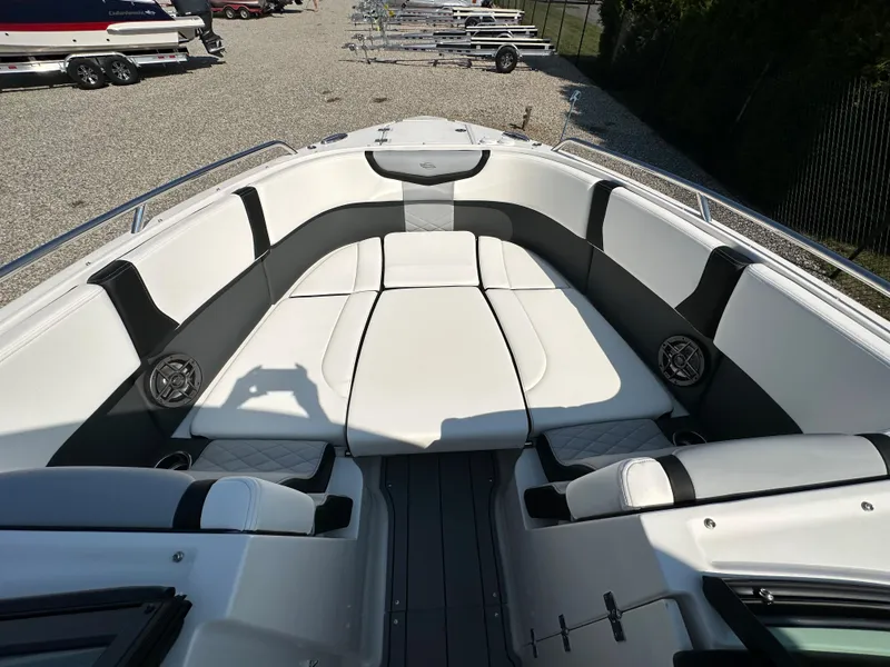 Slide: The Image of 2023 Chaparral 270 OSX boat interior with white seating and speakers, parked on gravel. - 16