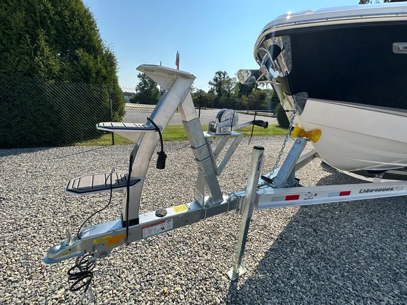 Slide: The Image of 2023 Chaparral 270 OSX boat on trailer, parked on gravel, with clear blue sky. - 3