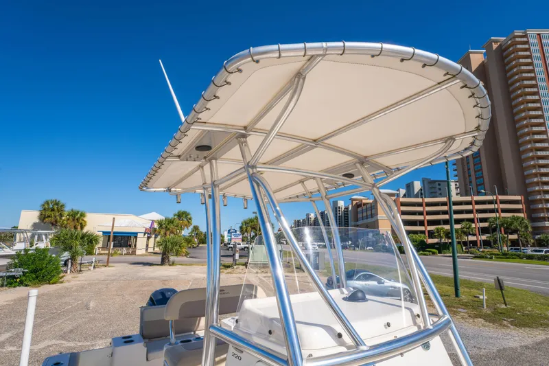 Slide: The Image of 2017 Cobia 220 Center Console boat with T-top, parked near buildings and palm trees. - 28