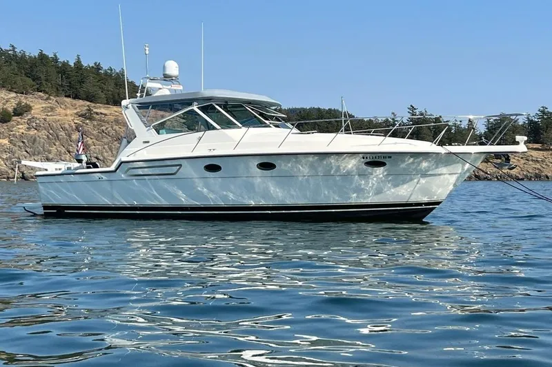 The Image of 1997 Tiara Yachts 3700 Open boat anchored on calm water near rocky shoreline. - 0