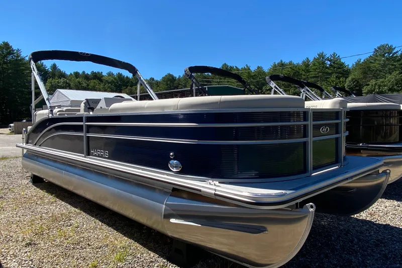 Slide: The Image of 2023 Harris Cruiser 250 pontoon boat parked on gravel lot under clear blue sky. - 4